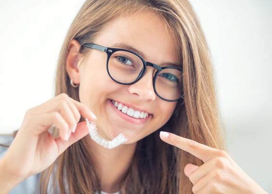 Teen pointing to her smile and holding Invisalign in Annapolis