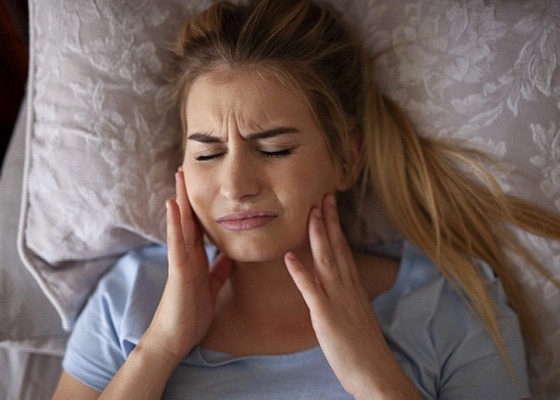 A young woman lying in bed holding both sides of her jaw and in need of TMJ Therapy in Annapolis