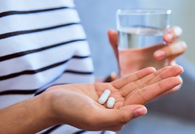 Person in striped shirt holding pill and glass of water