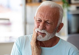 Man sitting on couch and rubbing jaw in discomfort