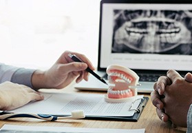 Hands at desk with model teeth, toothbrush, X-ray of jaw, and paperwork