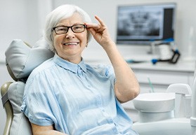 Senior woman sitting in dental chair and adjusting glasses