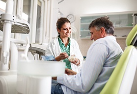 Smiling dentist showing patient model of teeth