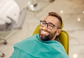 Man with glasses smiling while sitting in treatment chair