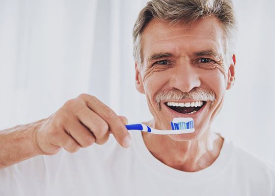 older man in white T-shirt brushing his teeth 
