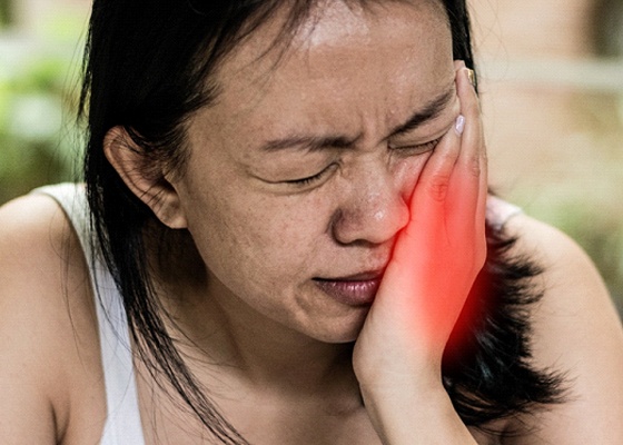 A young woman cringing in pain and holding her cheek with her hand that looks red to signify pain
