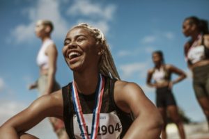 track runner smiling and sitting down with a metal around their neck