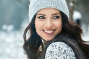 Woman in grey winter hat and grey sweater looking over her shoulder and smiling