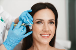 Smiling woman getting botox injection near her eye