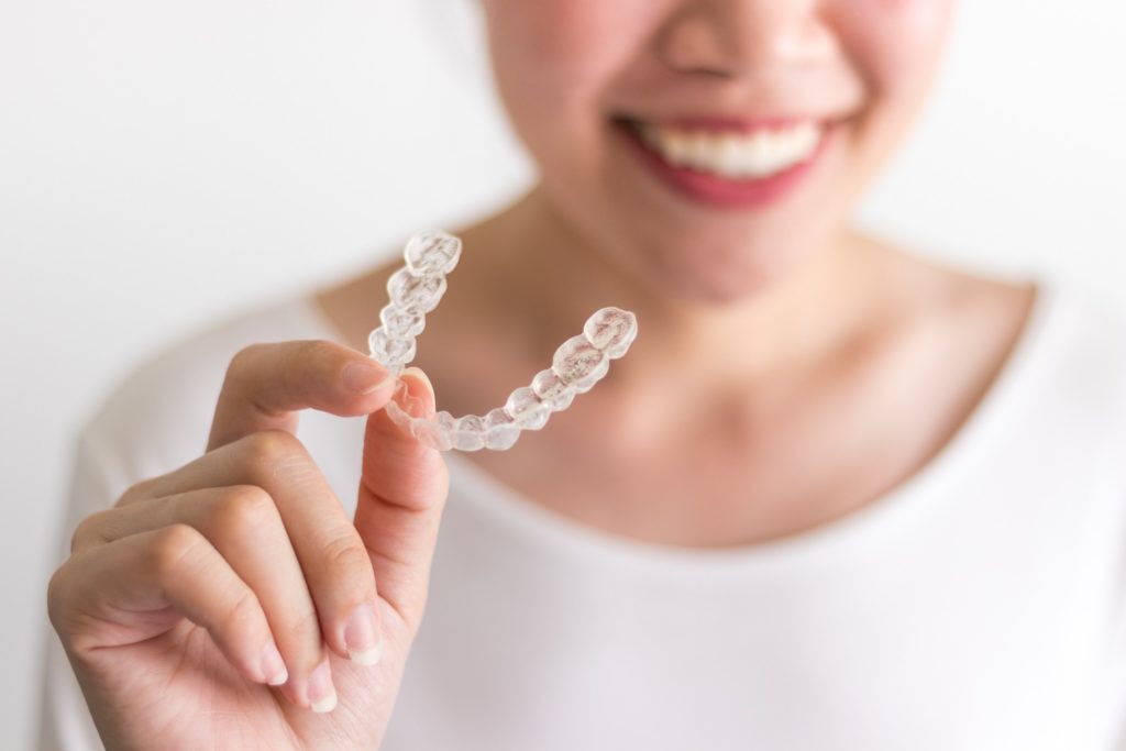 Smiling patient holding up Invisalign aligner